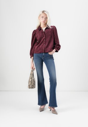 Bordeaux korduroy overhemd met pofmouwen, gecombineerd met aansluitende blauwe flared jeans. Accesoires zijn een handtas met patroon en hoge hakken.