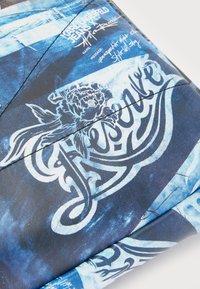 Läderplånbok med ett mönster av blå batik, intrikata blommor och skriftsnitt, samt kontrasterande mörka accenter.