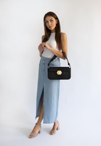 Gonna maxi in denim con uno spacco frontale, abbinata a una canotta bianca aderente. Borsa nera con un accento oro esagonale e sandali beige con tacco.