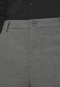 Pantaloni grigi su misura caratterizzati da una texture liscia, chiusura con bottone e tasche frontali. La vita è piatta con un sottile dettaglio di cucitura.