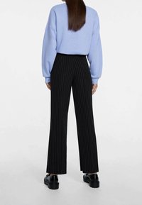 Lichtblauwe oversized sweatshirt gecombineerd met zwarte gestreepte wijde broek en stevige zwarte schoenen. De outfit heeft een relaxte pasvorm en zachte stof.