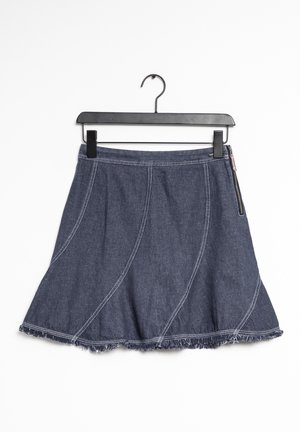 Gonna di jeans con cuciture bianche, orlo sfrangiato e cerniera laterale appesa a una gruccia con clip nera su sfondo bianco.