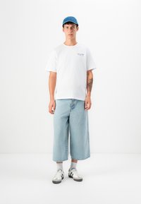 White cotton t-shirt with blue text, light blue denim culottes, and gray and white sneakers. Blue cap completes the outfit.
