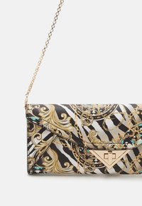 Clutch-Tasche mit schwarz-weiß-goldenem Barock- und Kettenmuster, goldfarbenem dreieckigem Verschluss und dünnem goldfarbenem Kettenriemen.