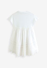 Hvid bomulds kjole med korte ærmer, indsnævret talje og broderet blonderkant ved skørtets kant. Glat tekstur, knælængde design.