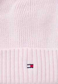 Bonnet tricoté rose avec une texture côtelée, arborant un petit logo brodé en rouge, blanc et marine sur le revers. Matière douce et extensible.