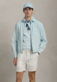 Jachetă albastră deschisă, șapcă asortată și cămașă albastră deschisă cu pantaloni scurți albi. Având un design simplu, ținuta pune în evidență texturi și culori delicate.