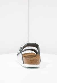 Sølv bagside af en sandal med en korksål, justerbare stropper og en hvid gummiydersål. Designet inkluderer en sløjfe-accent.
