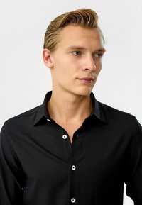 Zwarte overhemdd met een klassieke kraag. Kenmerkt zich door witte knopen en een gladde stof. Tailored fit, geen patronen of accenten.