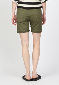 Olivgröna bomullsshorts med uppvikta ben, som har bakfickor och en mjuk textur. Modellen bär svarta sandaler.