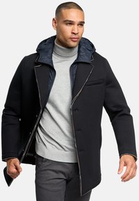 Black overcoat with a puffy navy hood, light gray turtleneck underneath, and gray pants. Features button closure and contrasting stitching.