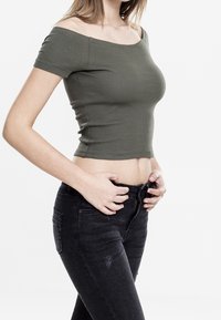 Olivově zelený žebrovaný crop top s krátkými rukávy, zkombinovaný s černými džíny s vysokým pasem a jemnými detaily opotřebení.