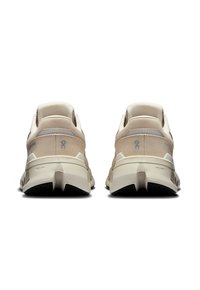 Zapatillas deportivas beige con parte superior de malla texturizada y acentos suaves. La suela presenta un patrón de banda multidireccional para un mejor agarre.