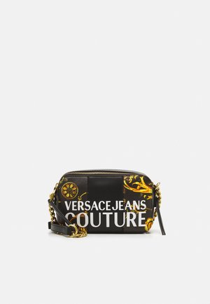 Sac bandoulière noir Versace Jeans Couture avec motifs baroques dorés, texte du logo blanc, chaîne dorée et fermeture éclair.