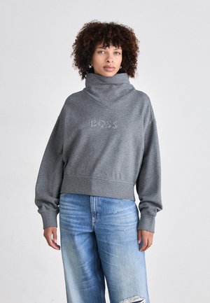 Grå cropped sweatshirt med høy krage, med en subtil "BOSS"-logo i midten. Kombinert med lyseblå ujevn jeans.