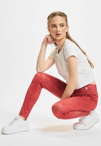 Leggings rossi con un motivo floreale, dotati di un alto girovita e logo bianco. Abbinati a una t-shirt bianca a maniche corte e sneaker bianche.