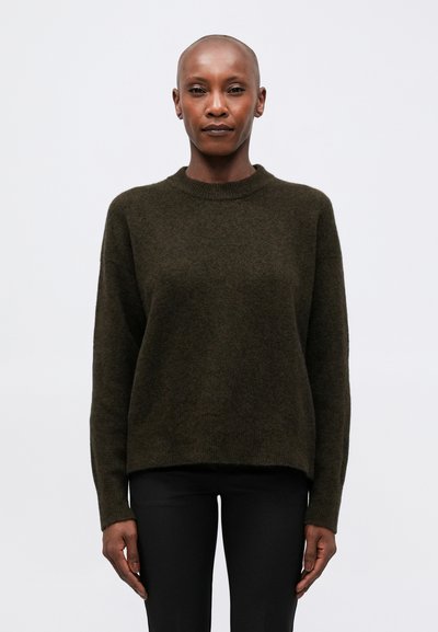 Pull olive vert, texture douce, col rond, manches longues, coupe légèrement ample. Associé avec un pantalon noir.