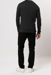 Schwarzes Langarm-T-Shirt mit rundem Halsauschnitt, kombiniert mit schwarzen Hosen und weißen Turnschuhen. Glatte Baumwolltextur, minimales Design.