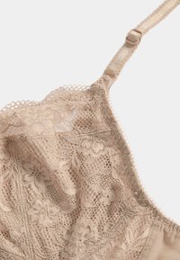 Bralette de encaje en color beige, con motivos florales, un delicado borde festoneado, tirantes ajustables y un acabado suave y texturizado.