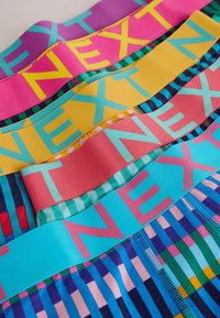 Colorful elastic bands with "NEXT" printed in large letters. Features bright colors: purple, pink, yellow, and blue with striped patterned fabric.