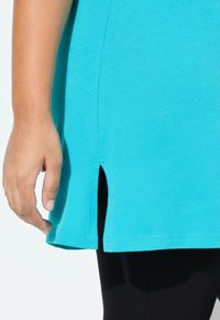 Haut en coton turquoise caractérisé par une coupe droite avec des fentes sur les côtés à l'ourlet, complété par une texture lisse et un minimum de détails de couture.