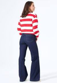 Rood-wit gestreepte gebreide trui gecombineerd met donkerblauwe uitlopende denim broek. De broek heeft gestikte zakken en een gladde textuur.