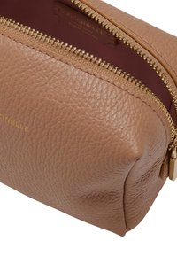 Hnědá texturovaná kožená kosmetická taštička s zlatým zipem, zlatými kovovými prvky a vínově červeným vnitřním podšívkou. Logo je vyraženo na kůži.