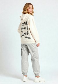 Felpa beige con la scritta "AMOUR" stampata in nero; abbinata a pantaloni cargo grigi chiari con tasche laterali; sneakers bianche completano il look.