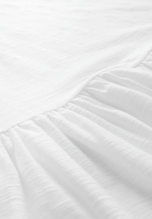 Tissu blanc avec une texture froissée, affichant un bord froncé. Matériau doux et léger, idéal pour la literie ou les rideaux.