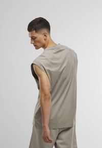 Light gray sleeveless shirt in soft fabric with a relaxed fit. Features a round neckline and dropped armholes for easy movement.
