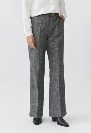 Pantalons larges gris texturés avec deux plis à l'avant ; portés avec une blouse blanche. Comprend des poches latérales et une taille haute.