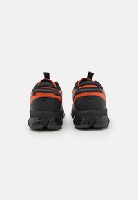 Baskets de sport noires et orange avec une tige en maille texturée et une semelle noire rembourrée. Dispose d'une languette à l'arrière pour un enfilage facile.