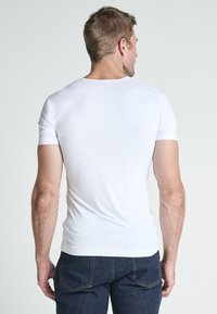 Vit kortärmad T-shirt i ett mjukt tyg, med rund halsringning och slim fit, kombinerad med mörka denimjeans. Bakifrån visad.