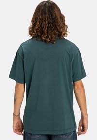 Grünes Baumwoll-T-Shirt mit kurzen Ärmeln, Rundhalsausschnitt und lockerer Passform. Hat ein schlichtes Design auf der Rückseite und leicht überschnittene Schulternähte.