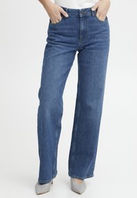 Vaqueros de tiro alto y pierna recta en denim azul oscuro. Cuenta con bolsillos frontales, lazos para cinturón y un cierre clásico de botón. Textura suave.