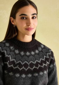 Chunky Strickpullover in Grautönen und Schwarz. Mit einem strukturierten, gemusterten Schultereinsatz und einem ribbeligen Kragen. Weicher, warmer Stoff.