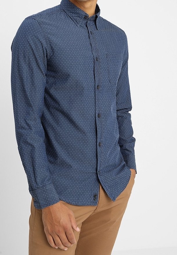 Sjöblå knäppskjorta med små vita prickar, spetsig krage, långa ärmar och en bröstficka. Mjuk tyg med en slät textur.