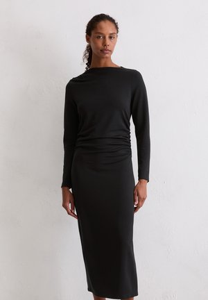 Zwarte jurk met lange mouwen en een bootnek, ruches bij de taille en een aangesloten silhouette dat tot halverwege de kuit reikt. Glad textuur van de stof.