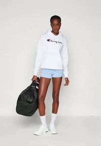 Valge kapuutsiga sviiter, millel on "Champion" logo, helesinised lühikesed püksid, must spordikott, valged sokid ja valged tossud neutraalsel taustal.