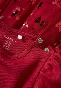 Rød kjole med sommerfuglemønstre og palietter, med en ribbet krave og trykknaplukning. Sammensætningsmærket er synligt ved halslinningen.