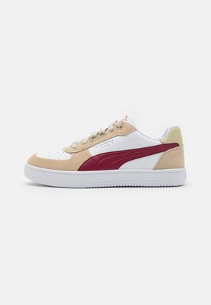 Niedriger Puma-Sneaker mit weißer Basis, beigen Velours-Overlays und einem burgunderfarbenen Seitenstreifen auf einer weißen Gummisohle, Seitenansicht auf einfarbigem Hintergrund.