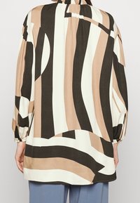 Košile s dlouhým rukávem z měkké látky, zdobená abstraktními pruhy v béžové, hnědé a krémové barvě, s nařaseným límcem a detaily na manžetách.