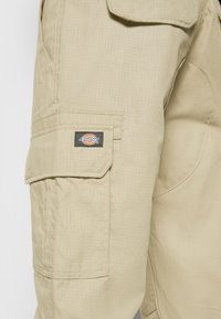 Béžové cargo kalhoty z texturované látky s boční kapsou a černou a barevnou nášivkou loga Dickies.