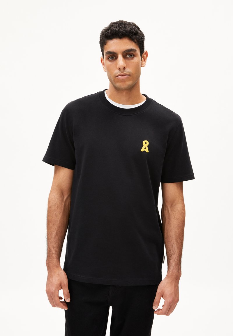 Zwarte katoenen t-shirt met een ronde hals en korte mouwen. Heeft een gele lintlogo op de linkerkant van de borst. Gladde textuur, ontspannen pasvorm.
