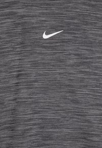 Šedé tkaninové tričko s textúrou s bielym logom Nike na hrudi. Vzor má jemné horizontálne pruhy.
