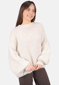 Übergroßer cremefarbener Strickpullover mit geripptem Ausschnitt und Bündchen. Weiche Textur und lockere Passform, mit Schulterabsätzen und weiten Ärmel.