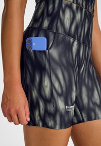 Svart och grönt mönstrade shorts med en sidoficka som håller en blå smartphone. Materialet verkar stretchigt och åtsittande, designat för aktivitet.