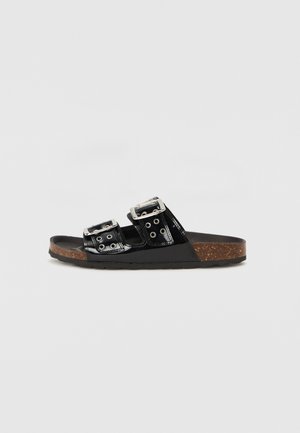 Svarta patenterade slip-in sandaler med två justerbara metallspännen, kork-mellansula, texturerad svart innersula och slitstark gummisula.