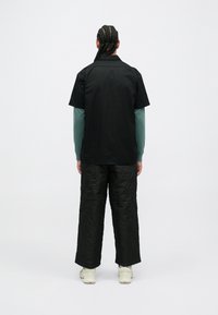 Černé tričko s krátkým rukávem přes tyrkysové tričko s dlouhým rukávem, zkombinované s prošívanými tmavými kalhotami a světlými teniskami, z pohledu zezadu.