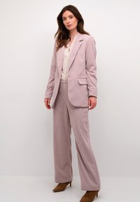 Traje de pana en color rosa claro con un blazer ajustado y pantalones de pierna ancha. La tela tiene una textura acanalada; combinado con una blusa color crema.